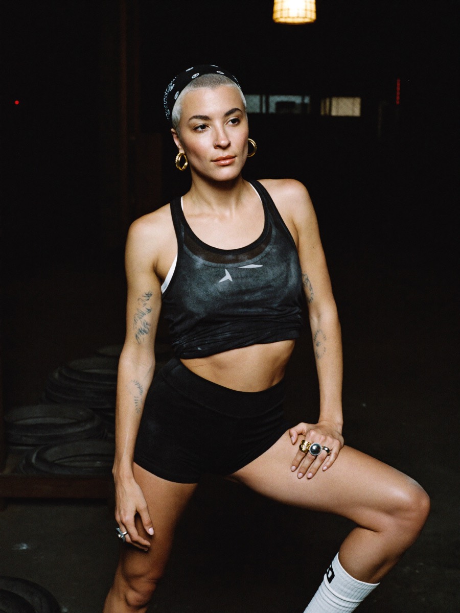 A woman sitting between sets in a dark gym, plates stacked behind her, mid session rather than posed
